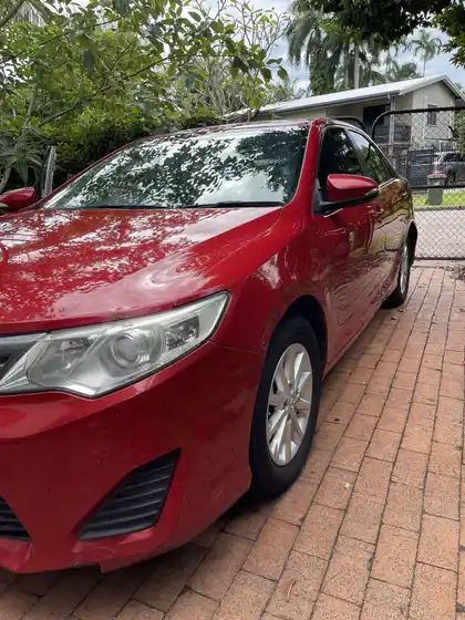 The same red Toyota Camry after detailing, the paint deep and wet-looking with sharp reflections