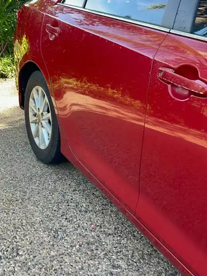 Side of a red Toyota Camry before detailing, the paint flat and hazy with dulled reflections