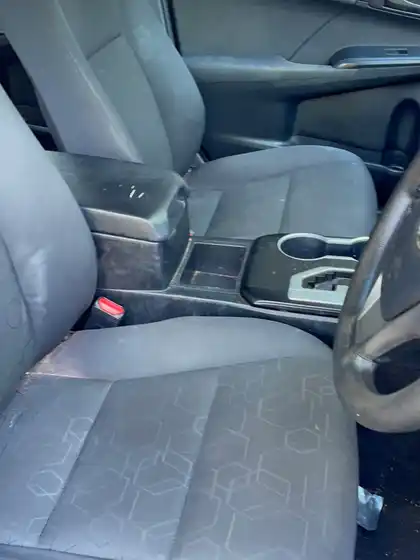 Driver seat and centre console of a Toyota Camry before detailing, the fabric soiled and the console dusty