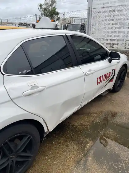 Driver side of a white taxi Camry with both doors and the rear quarter creased and scraped along their full length