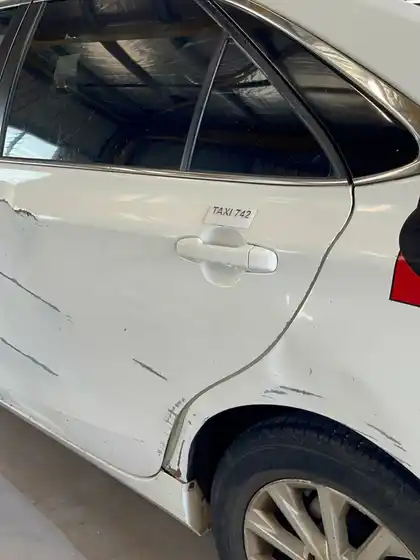 Rear door and quarter panel of a white Camry with a long horizontal crease and scraped paint above the wheel arch