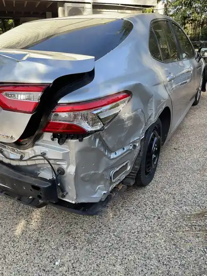 Rear of a silver Toyota Camry Hybrid after a rear-end collision, with the boot lid buckled, the rear bumper torn off and the quarter panel crushed