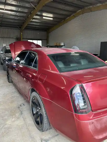 Rear three-quarter view of a red Chrysler 300S inside the workshop, its paint flat and uneven under the lights