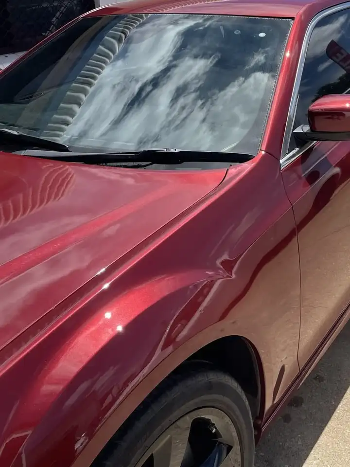 Bonnet, windscreen and front door of a red Chrysler 300S after refinishing, the metallic paint deep and evenly reflective in daylight