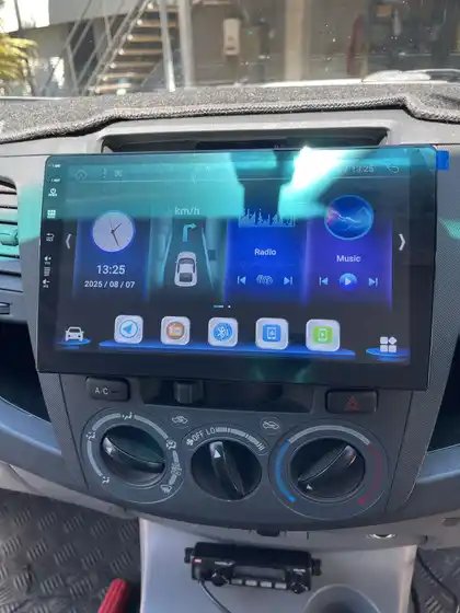 The same Hilux dashboard with a large touchscreen headunit fitted, showing the home screen with media and navigation