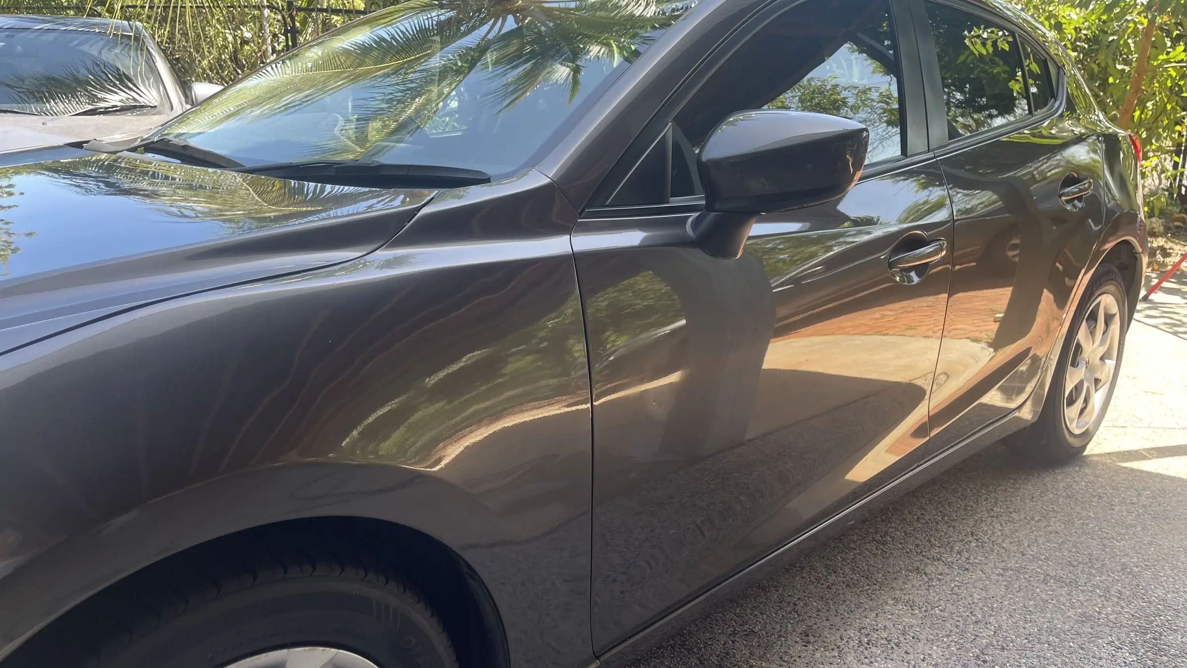 Finished dark-grey Mazda reflecting Darwin palm trees in its paintwork